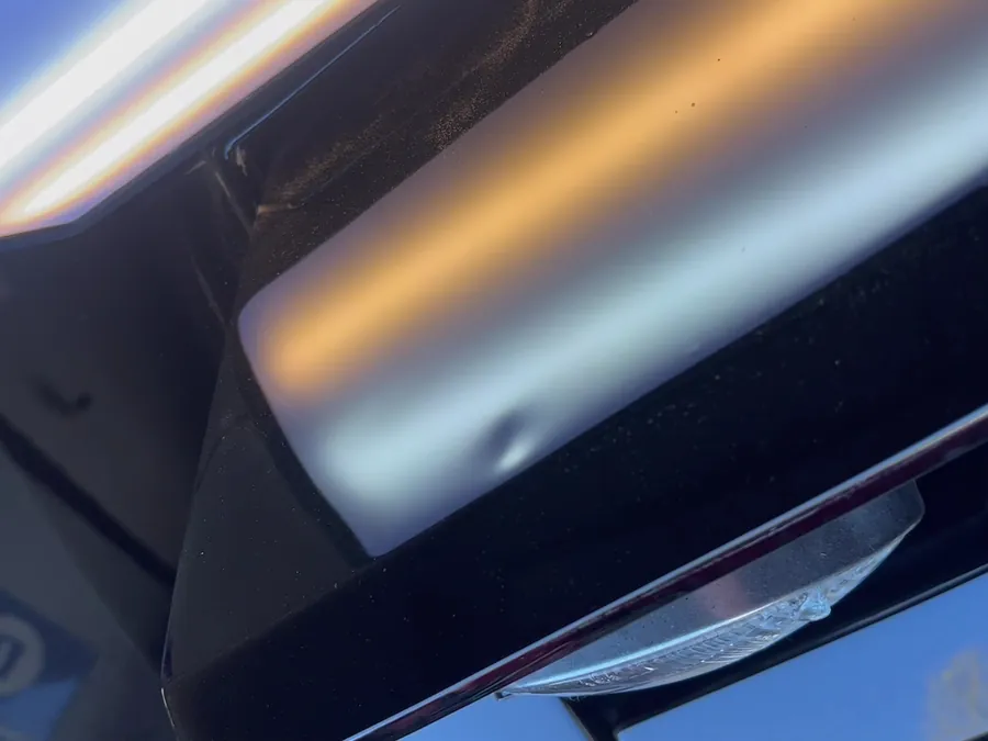A small dent showing in a light's reflection on a black panel