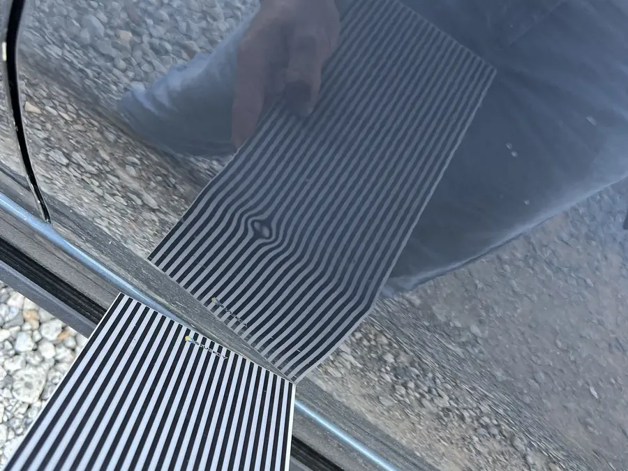 A striped line board reflected in a dark car door, the stripes bending into a small bullseye where the dent is